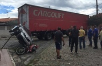 Ao fazer curva, carreta atinge veículo, que cai sobre moto